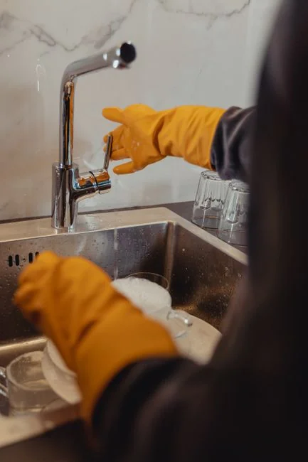Close-up of hand cleaning window with squeegee outdoors using yellow gloves.